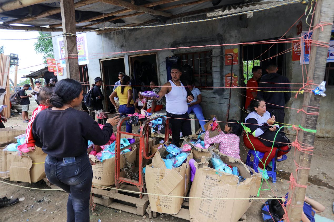 2023年9月23日,巴拿馬達連省拉哈斯布蘭卡斯移民接待站等待前往美國的移民,一名男子將捐贈的鞋子遞給一名懷著嬰兒的婦女。