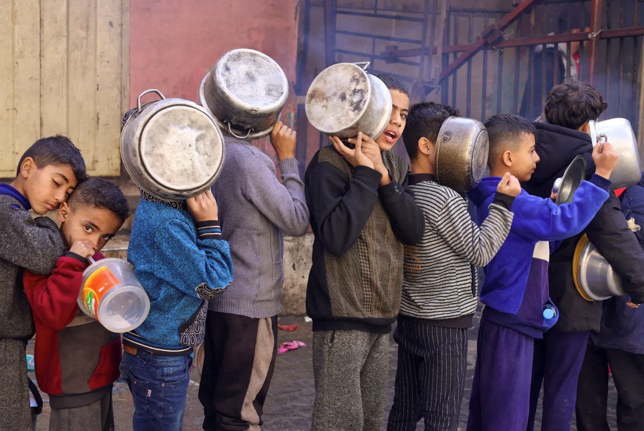 2023年12月14日,在加沙地帶南部的拉法,隨著以色列和哈馬斯之間的沖突持續,巴勒斯坦兒童拎著鍋排隊領取慈善廚房烹制的食物,沖突繼續導致糧食供應短缺。